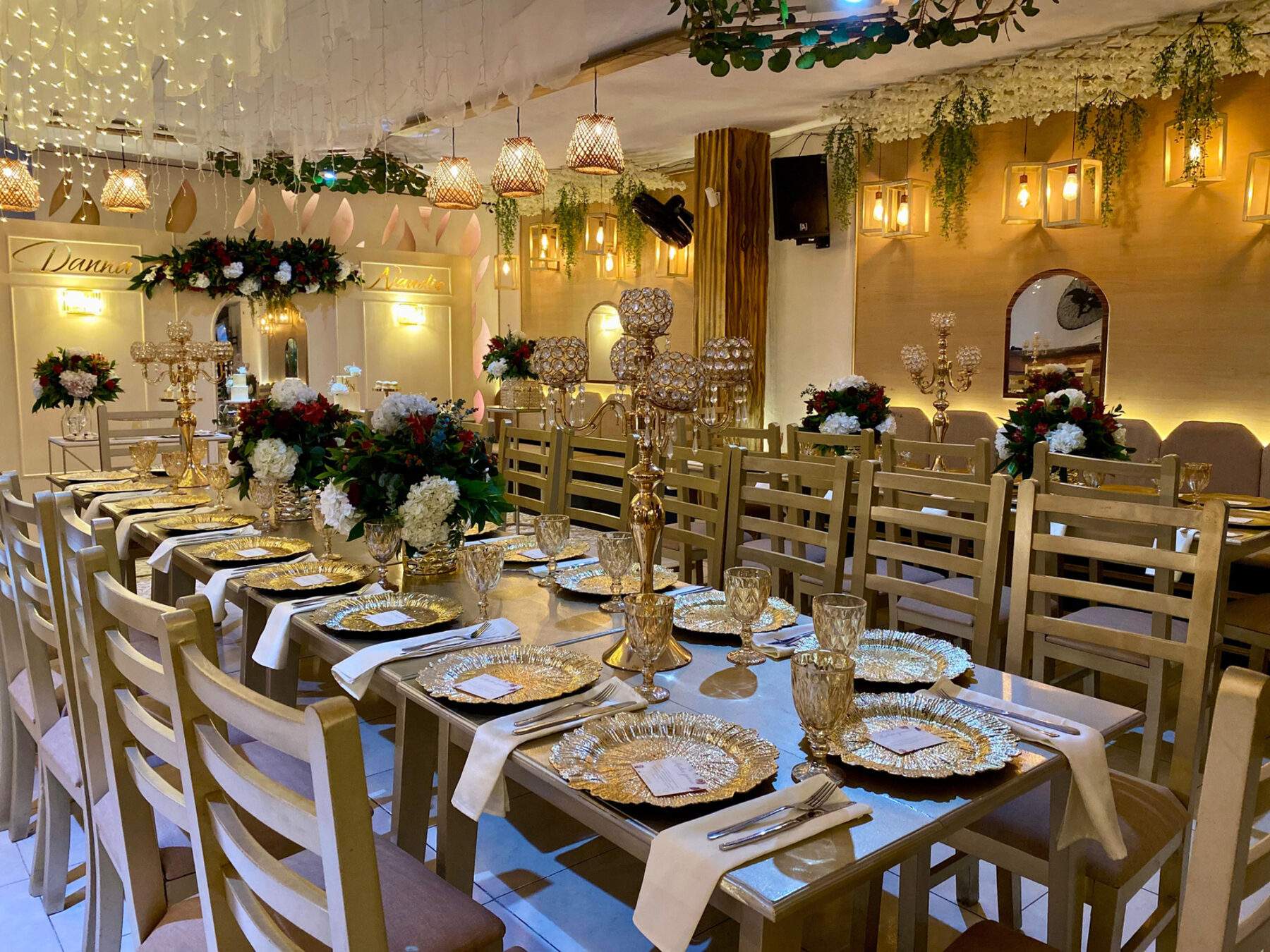 Mesa larga montada con vajilla dorada, flores y luces colgantes en el salón de Armonía Club